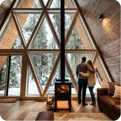 Interior with a wood stove and floor-to-ceiling glass facing the pines